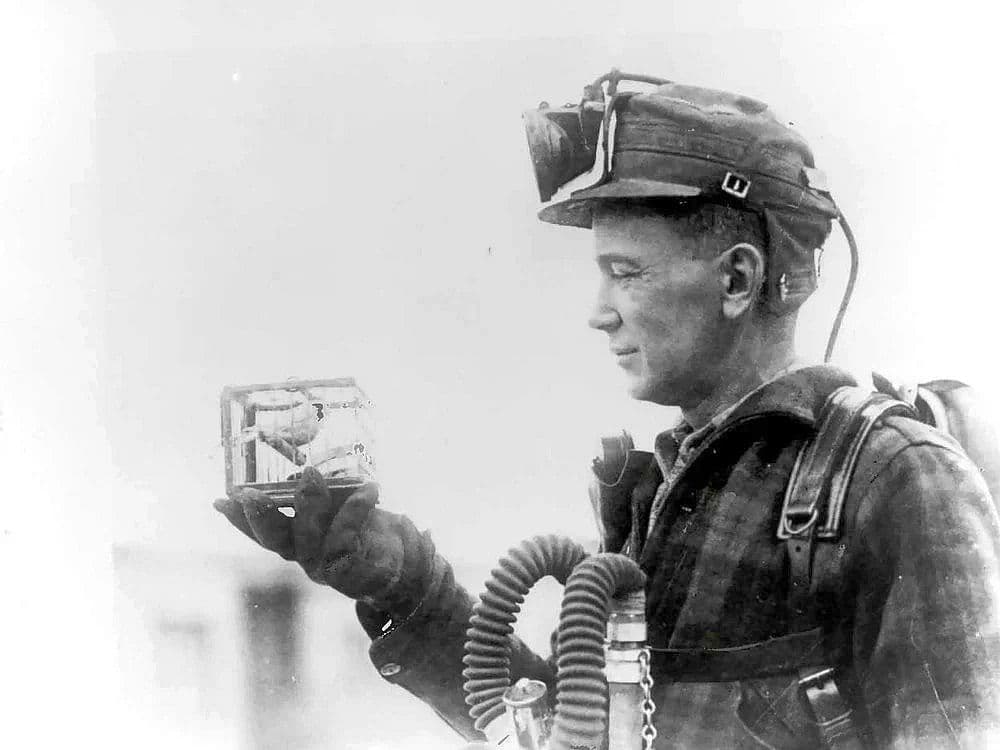 Historic black-and-white photo of a mine foreman holding a small cage with a canary